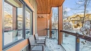 En træterrasse med fletstole, grill og udsigt over et sneklædt landskab.