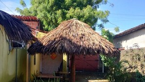A backyard with a thatched-roof structure, a small pool, and a tree.