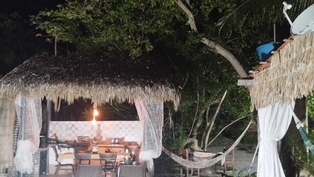 An outdoor pool area with a thatched-roof structure, lounge chairs, and a dining setup.