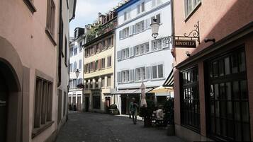 Eine schmale Straße mit Häusern an beiden Seiten, ein Schild mit 'BINDELLA' über einem Geschäft, und eine Person, die geht.