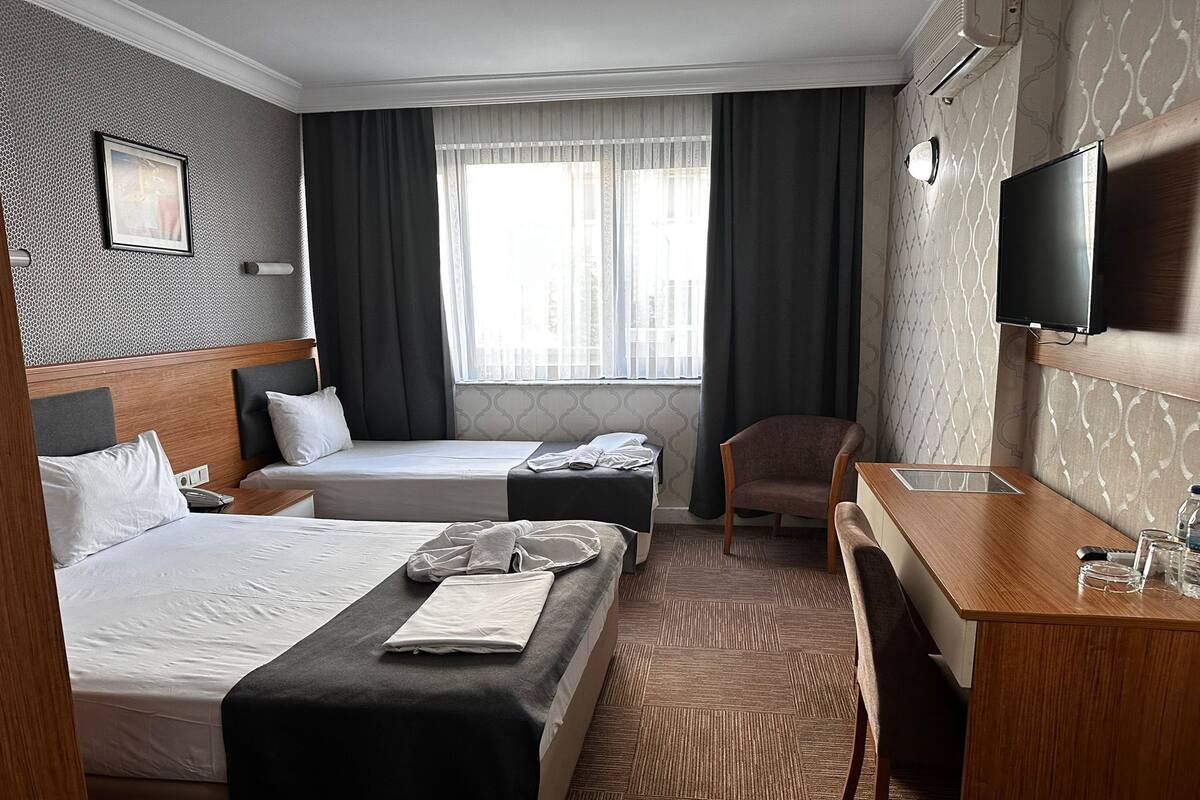 A hotel room with two beds, a desk, a chair, a TV, and a window with curtains.