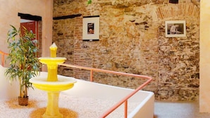 A room with a stone wall, a yellow pedestal fountain, and a potted plant. - Résidence St Vincent (Collioure)