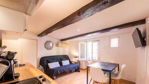 A compact living space with a kitchenette, a sofa, a dining table, and a TV mounted on the wall. - Résidence St Vincent (Collioure)