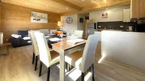 A modern interior with a wooden ceiling, a dining area with a table and chairs, a sofa, and a kitchen area with cabinets and appliances. - Gite Spacieux, Cosy, Tout Confort au Pied des Pistes (Septmoncel les Molunes)