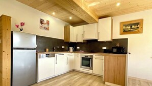 A modern kitchen with white cabinets, a stainless steel refrigerator, a built-in oven, and a microwave. - Gite Spacieux, Cosy, Tout Confort au Pied des Pistes (Septmoncel les Molunes)