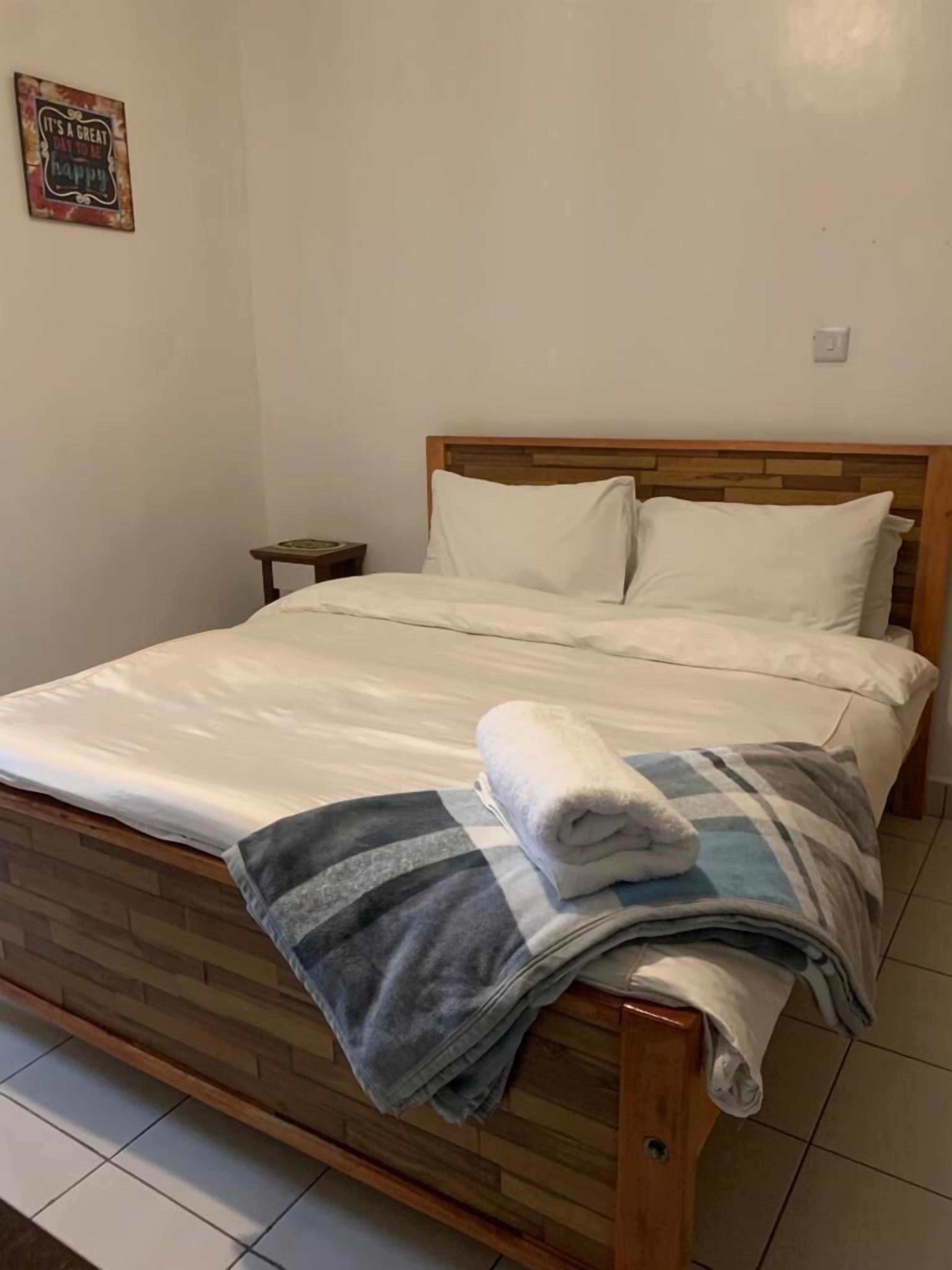 Una cama bien tendida con cabecera de madera, una mesita de noche pequeña y un adorno en la pared.