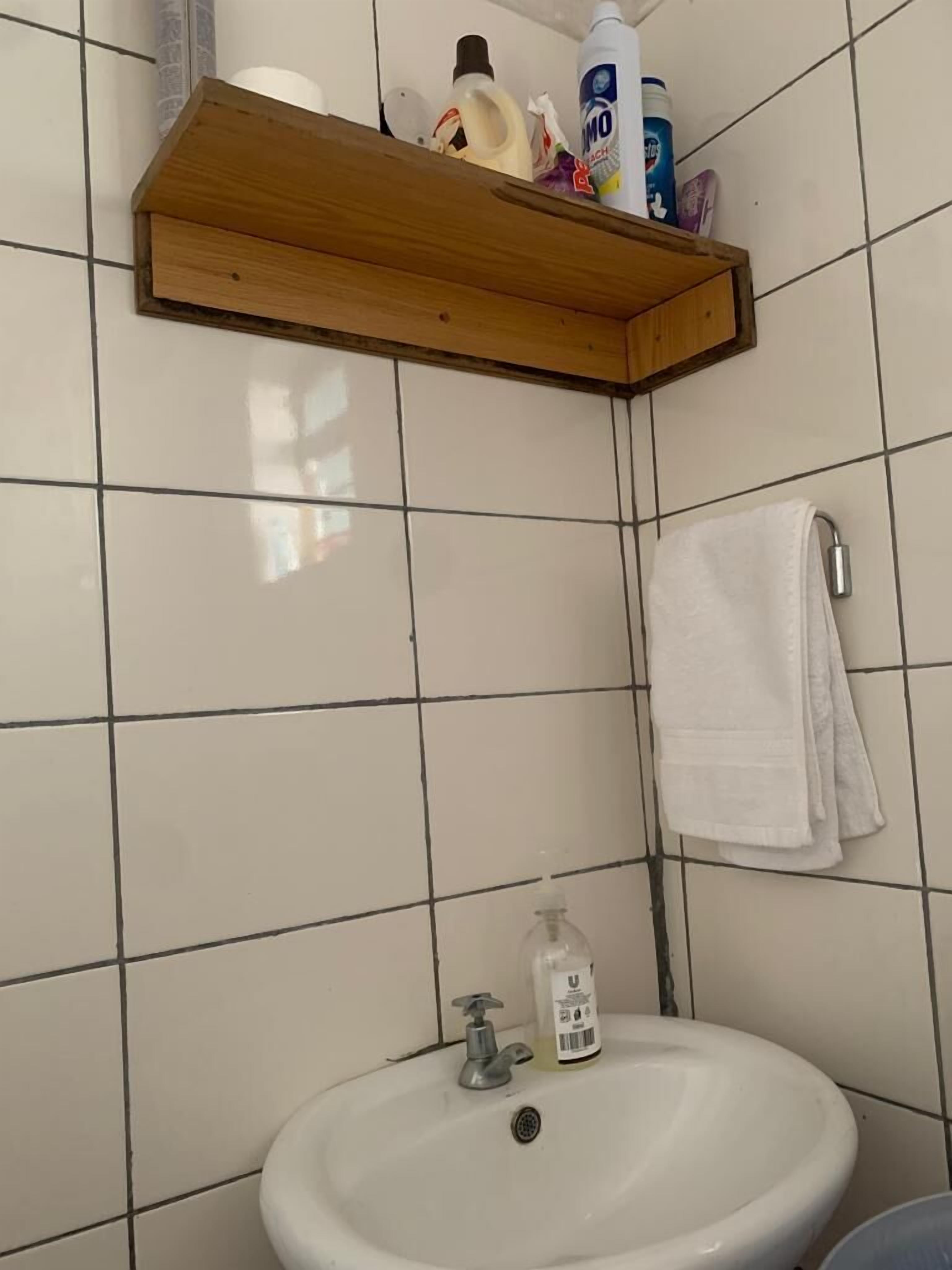 Un baño con un lavamanos blanco, un estante de madera encima y una toalla blanca colgada en la pared.