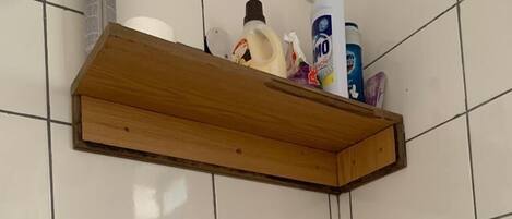 Une salle de bain avec un lavabo blanc, une étagère en bois au-dessus, et une serviette blanche accrochée au mur.