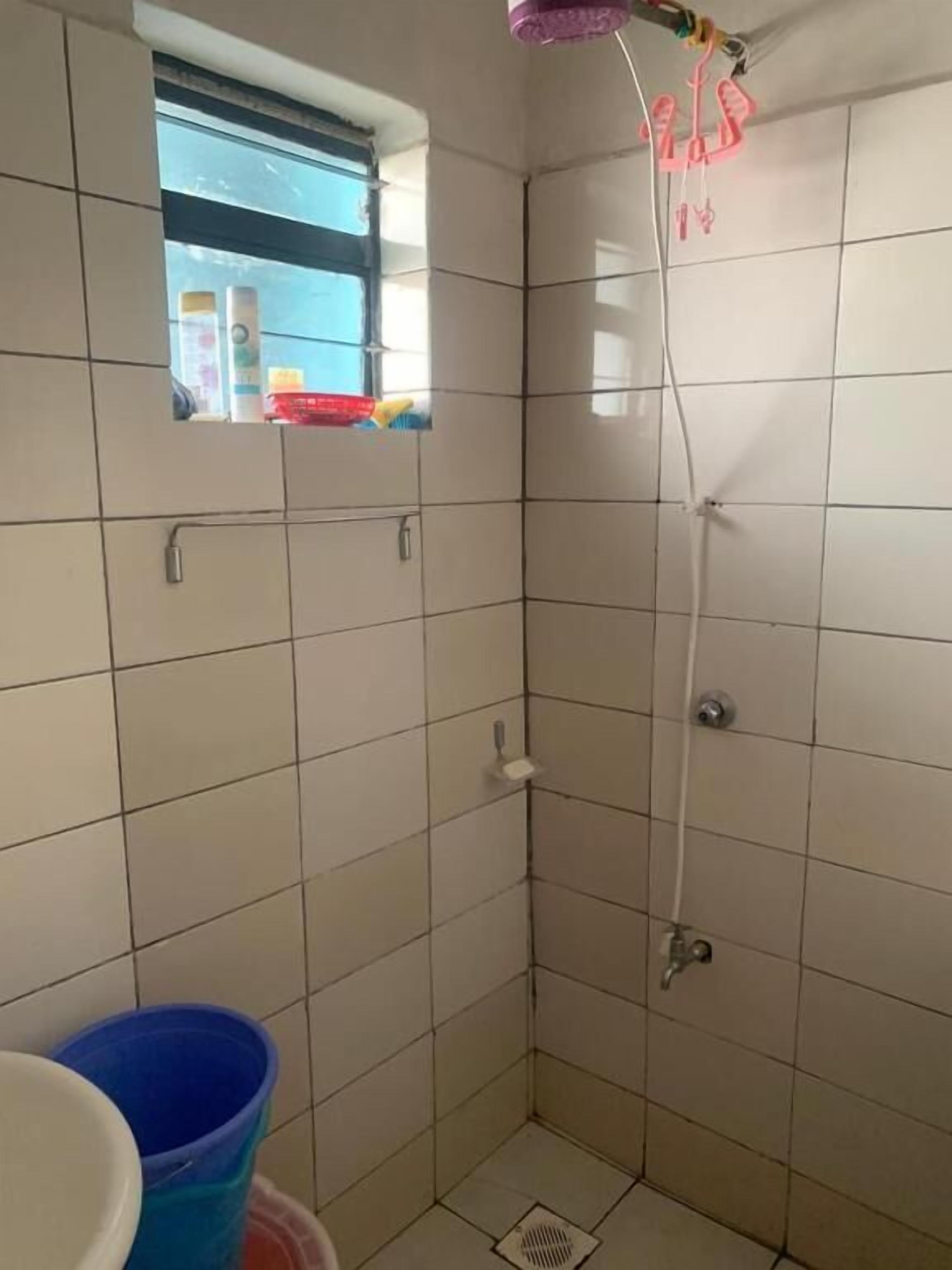 A small, tiled bathroom with a shower, a window, and a shelf with toiletries.