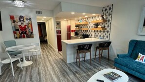 Una sala de estar moderna con un sofá azul, una mesa de centro blanca y una zona de cocina con un refrigerador rojo.
