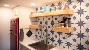 Una cocina con un refrigerador rojo, un lavamanos y estantes de madera arriba.