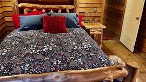 A wooden log cabin-style bedroom with a bed, pillows, a nightstand, and a door.