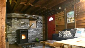 A cozy cabin interior with a stone wall, a fireplace, a sofa, and a wooden table.