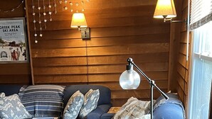 A cozy room with a blue sofa, two lamps, a wooden coffee table, and a window with blinds.