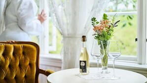 A table with a bottle of white wine, two wine glasses, and a vase with flowers. - Utne Hotel (Ullensvang)