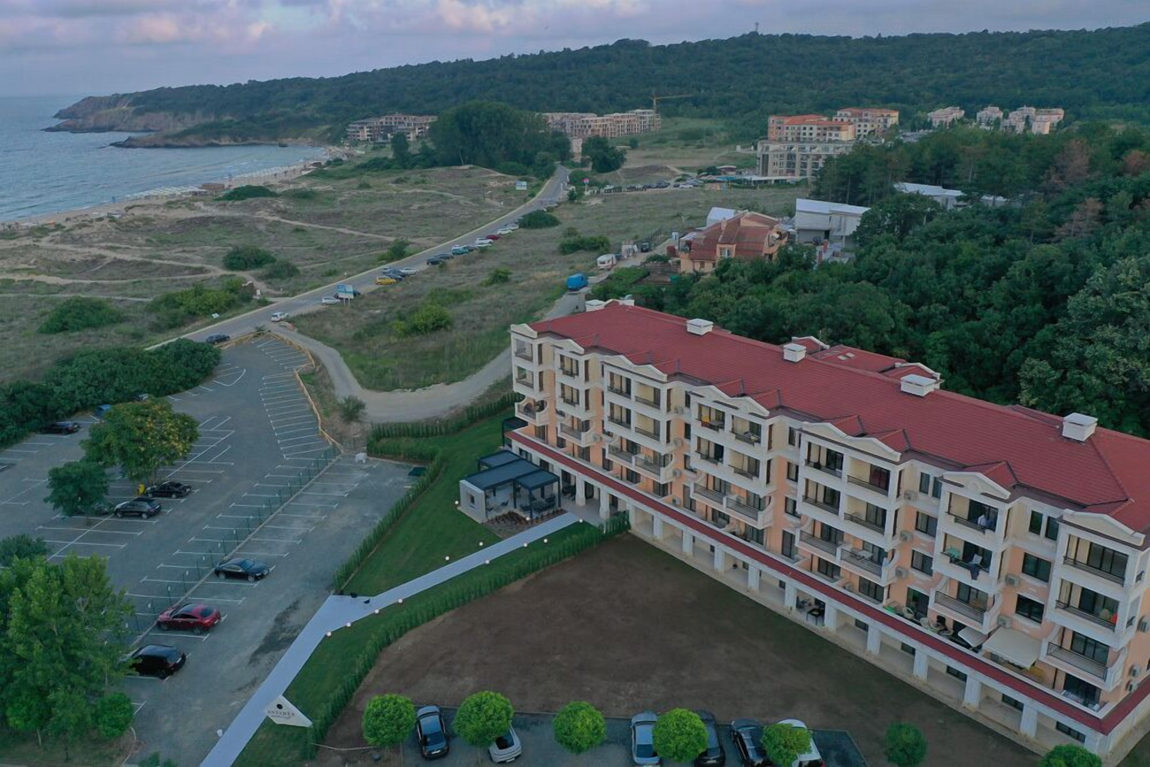 A multi-story building with a red roof, surrounded by greenery and a parking lot.