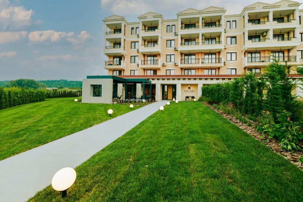 A multi-story hotel with a central entrance, surrounded by well-maintained lawns and a pathway leading to the entrance.