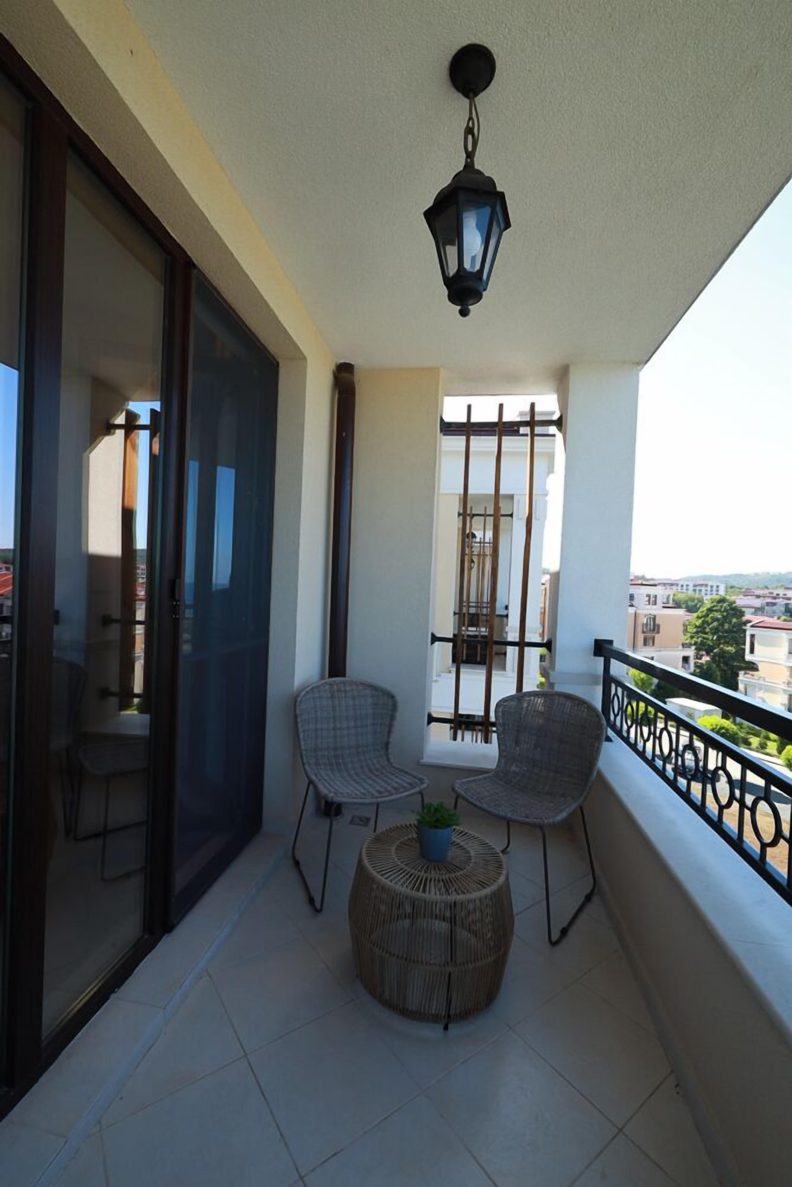 A balcony with two wicker chairs, a small round table with a plant, and a hanging lantern.