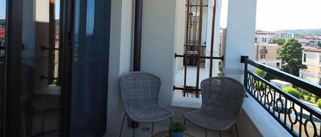 A balcony with two wicker chairs, a small round table with a plant, and a hanging lantern.