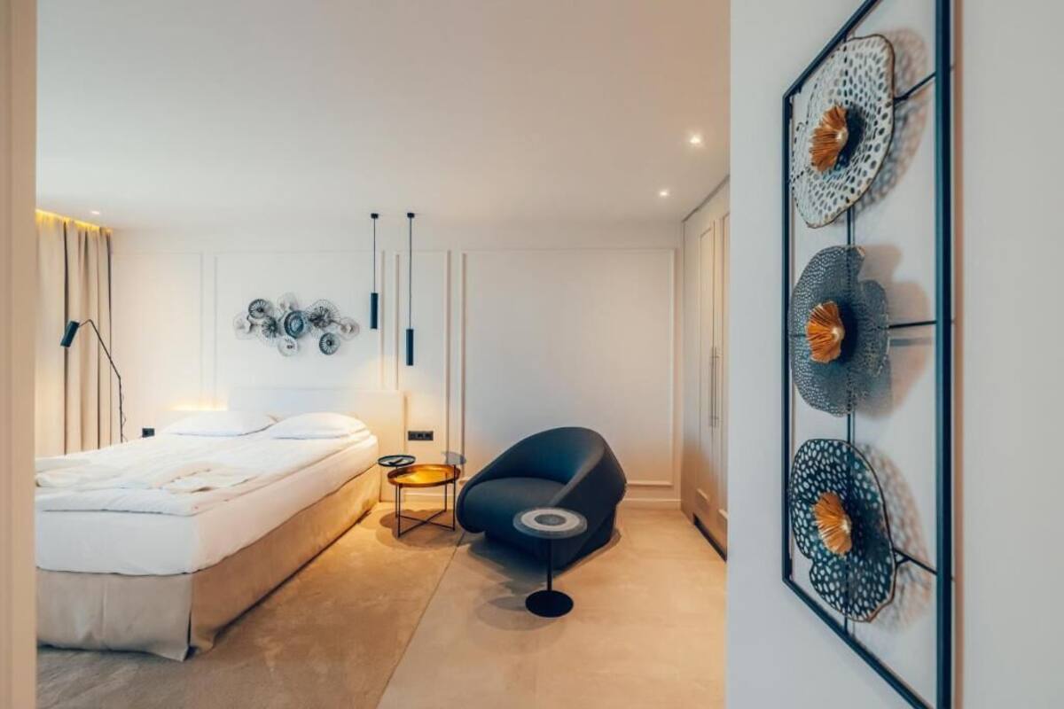 Un dormitorio moderno con cama, una silla, una mesita y decoración en la pared.