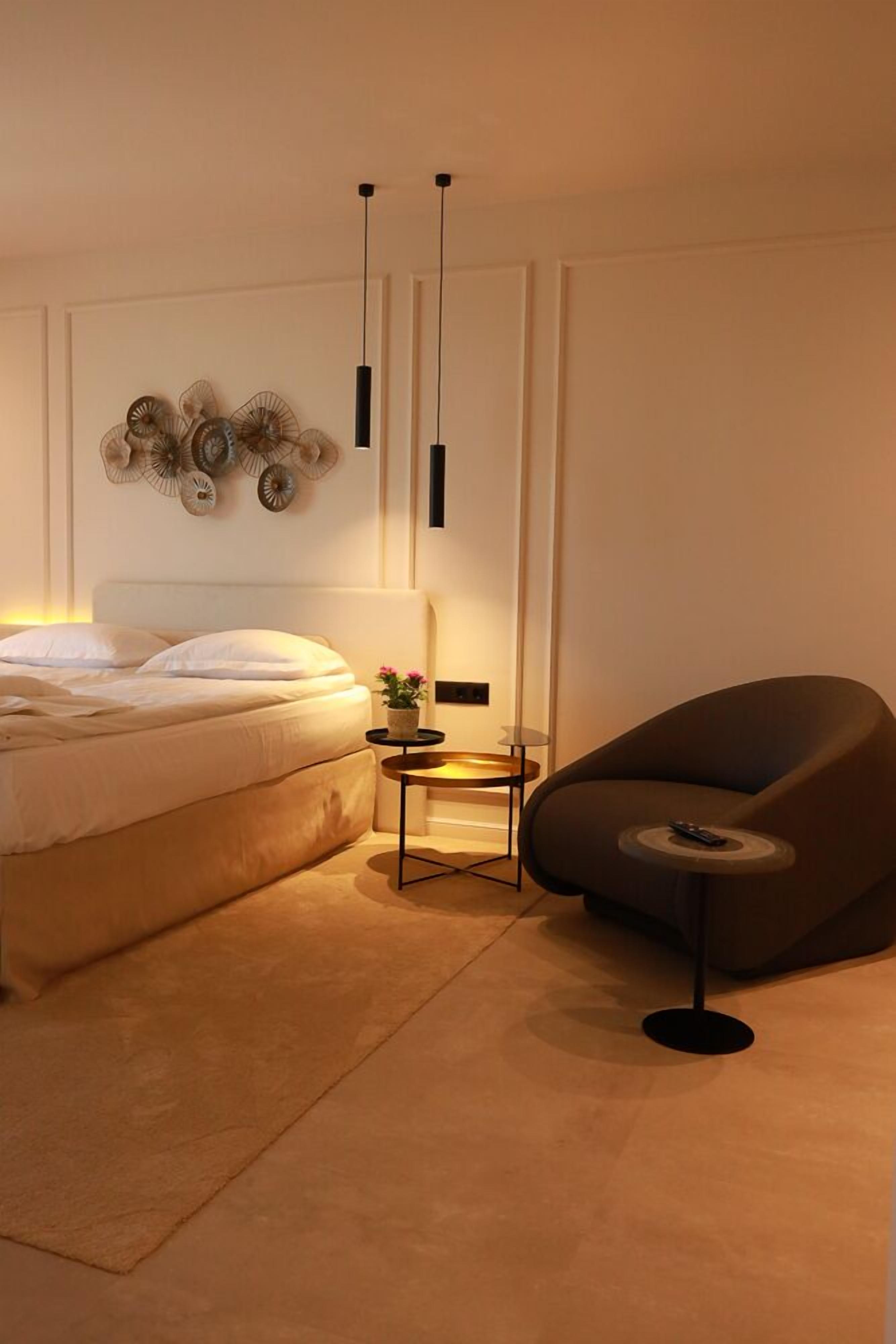 Een moderne slaapkamer met een bed, een nachtkastje met lamp, een decoratief wandobject en een bijzondere stoel.