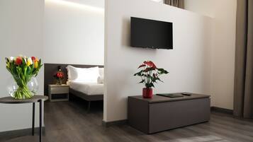 A modern hotel room with a bed, bedside table, TV, and a small desk with a potted plant.