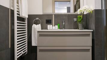 A modern bathroom with a white vanity, a towel rack, a mirror, and a vase with flowers.