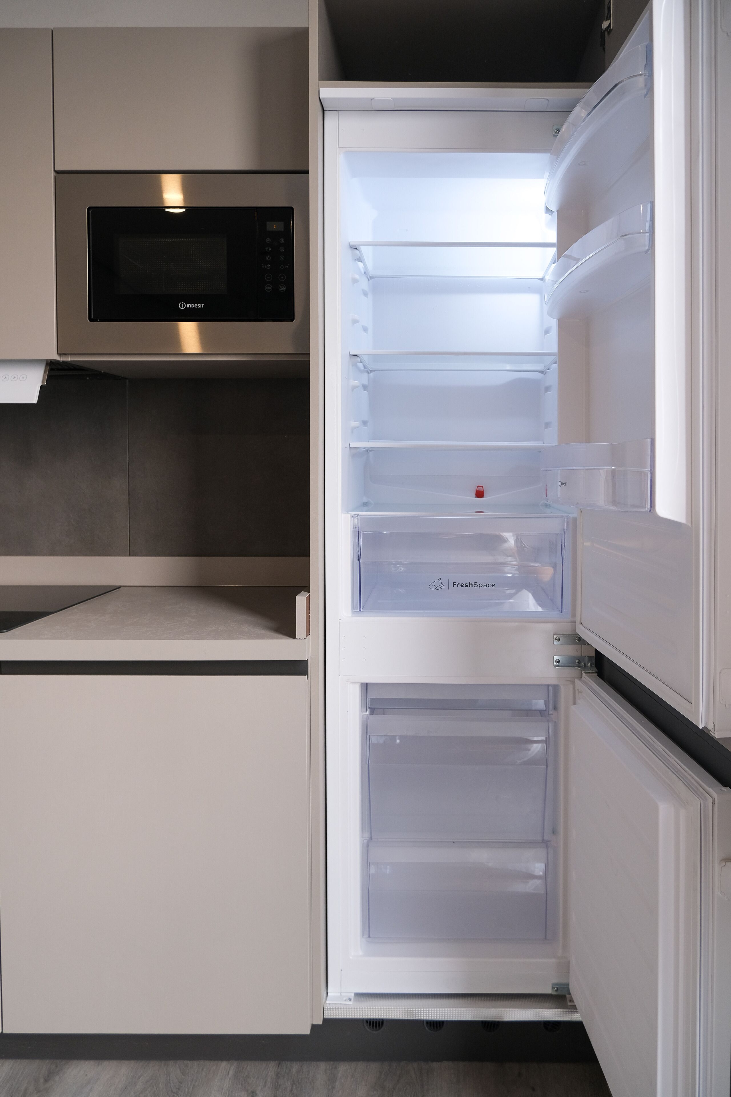 A modern kitchen with a built-in microwave and a white refrigerator with multiple compartments.