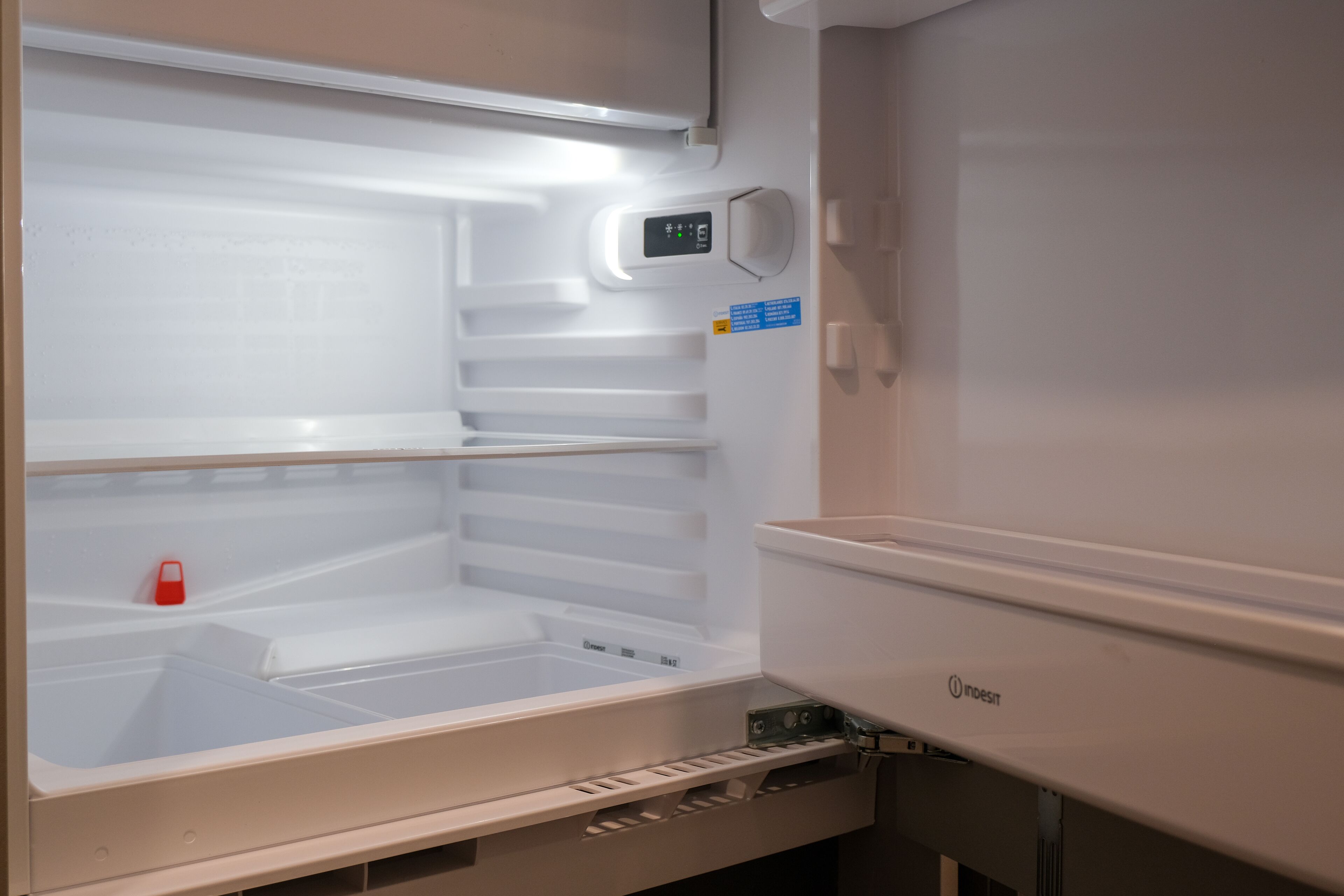An empty refrigerator with a digital control panel and a blue sticker on the door.