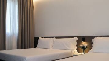 A hotel room with two beds, a nightstand with a vase of flowers, and a wall-mounted light.