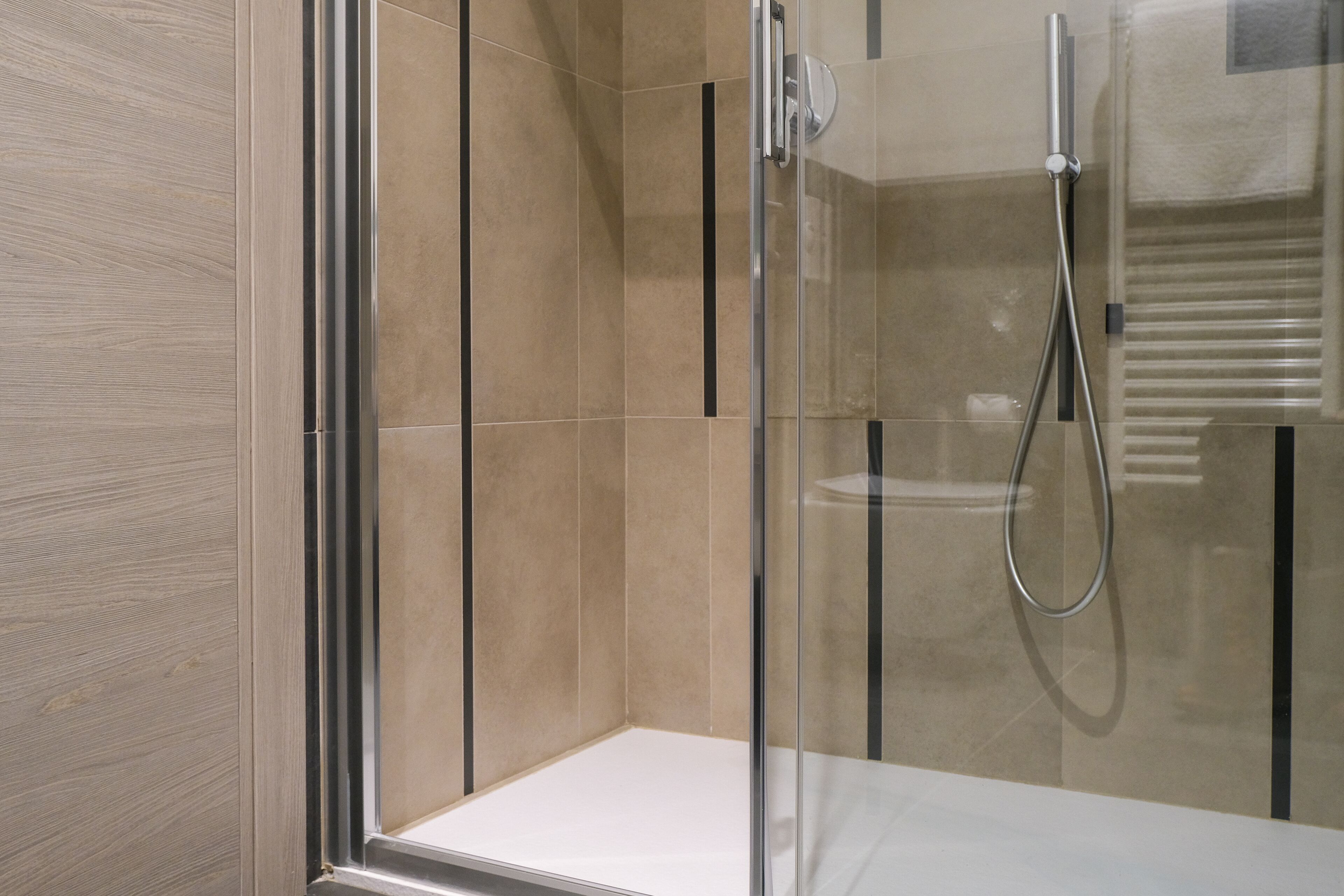 A modern shower enclosure with a glass door, a handheld showerhead, and a towel rack.