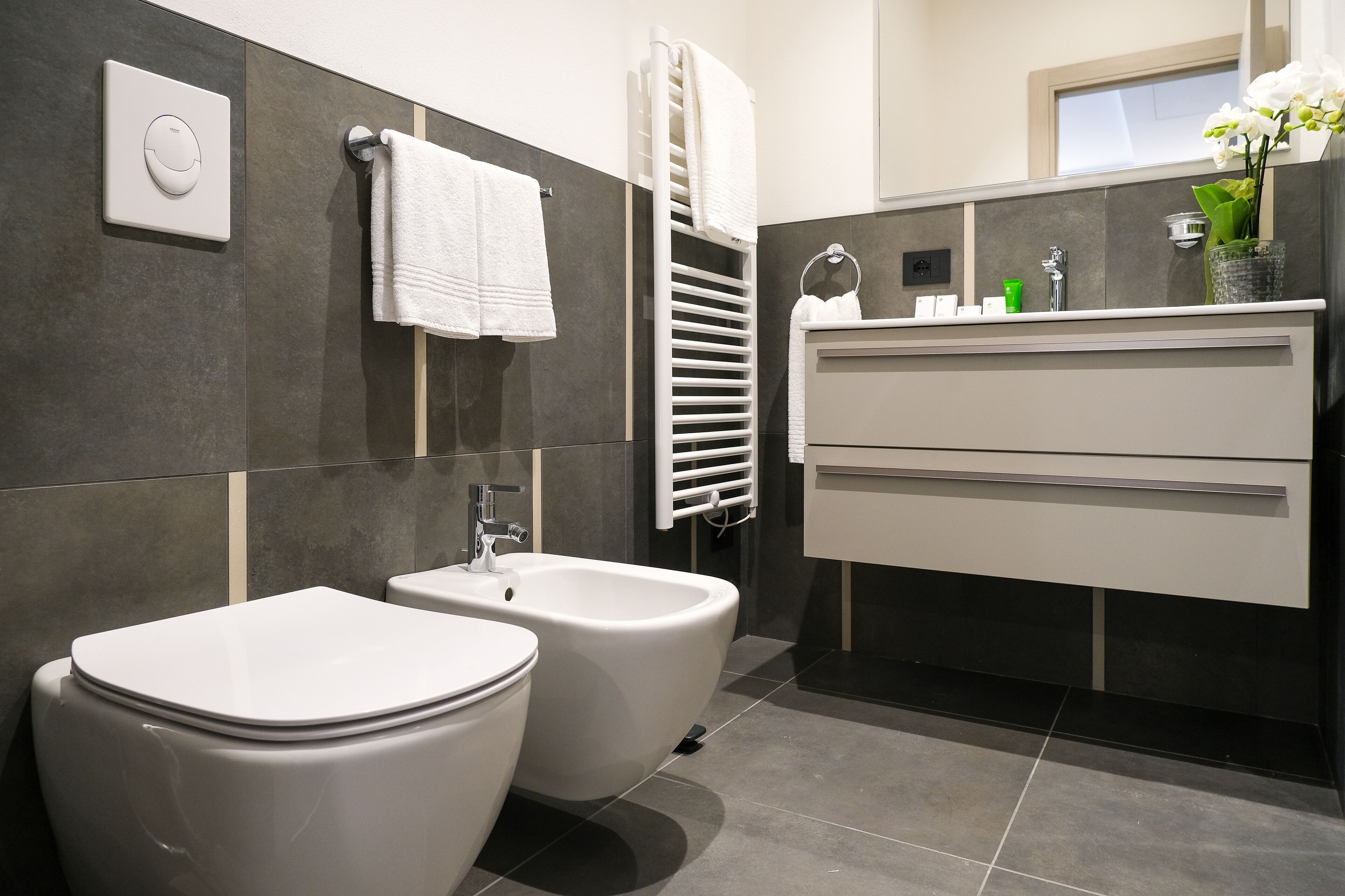 A modern bathroom with a bidet, toilet, and a vanity with a mirror and sink.