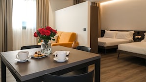 A hotel room with a dining table, two beds, and a vase of red roses. - Emerald Green Residence (Caldiero)