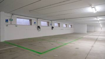 Un grand parking souterrain, vide, avec un sol en béton, des lignes vertes délimitant les places et de nombreuses fenêtres le long des murs.