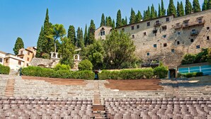 An outdoor amphitheater with stone steps and rows of seats, surrounded by trees and historic stone buildings. - Emerald Green Residence (Caldiero)