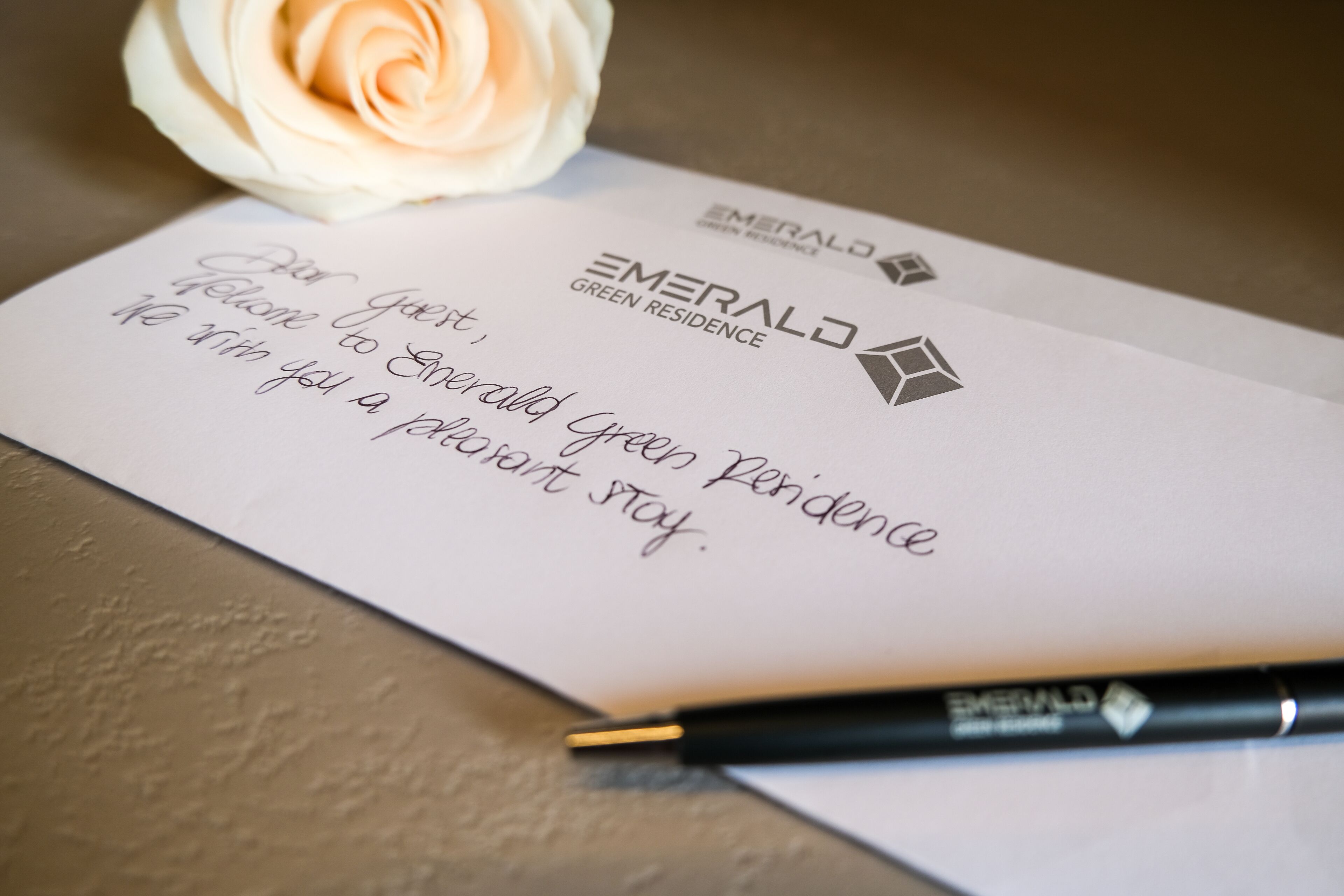 A welcome card from Emerald Green Residence with a black pen beside it.