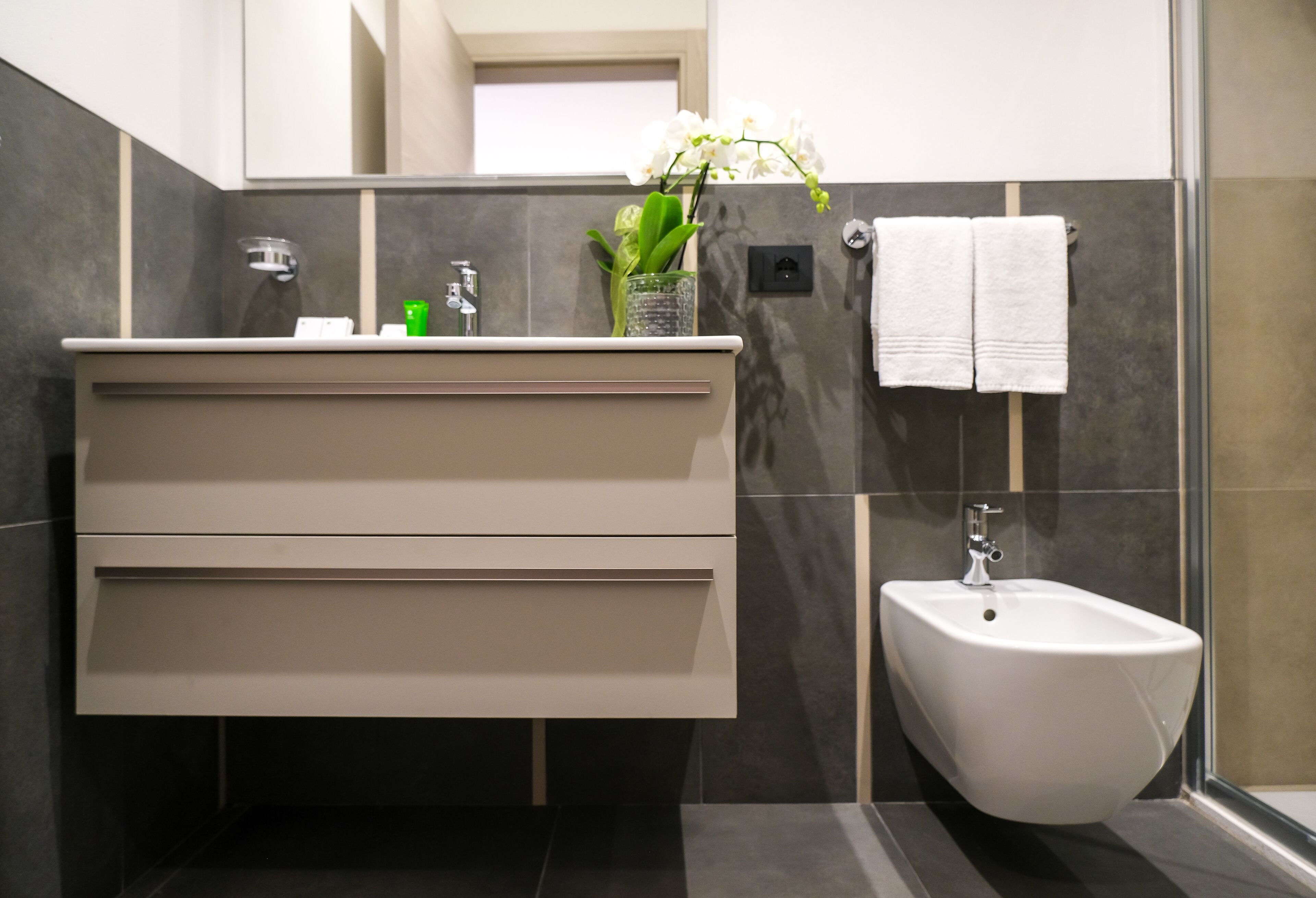 A modern bathroom with a vanity, bidet, and a vase with flowers.