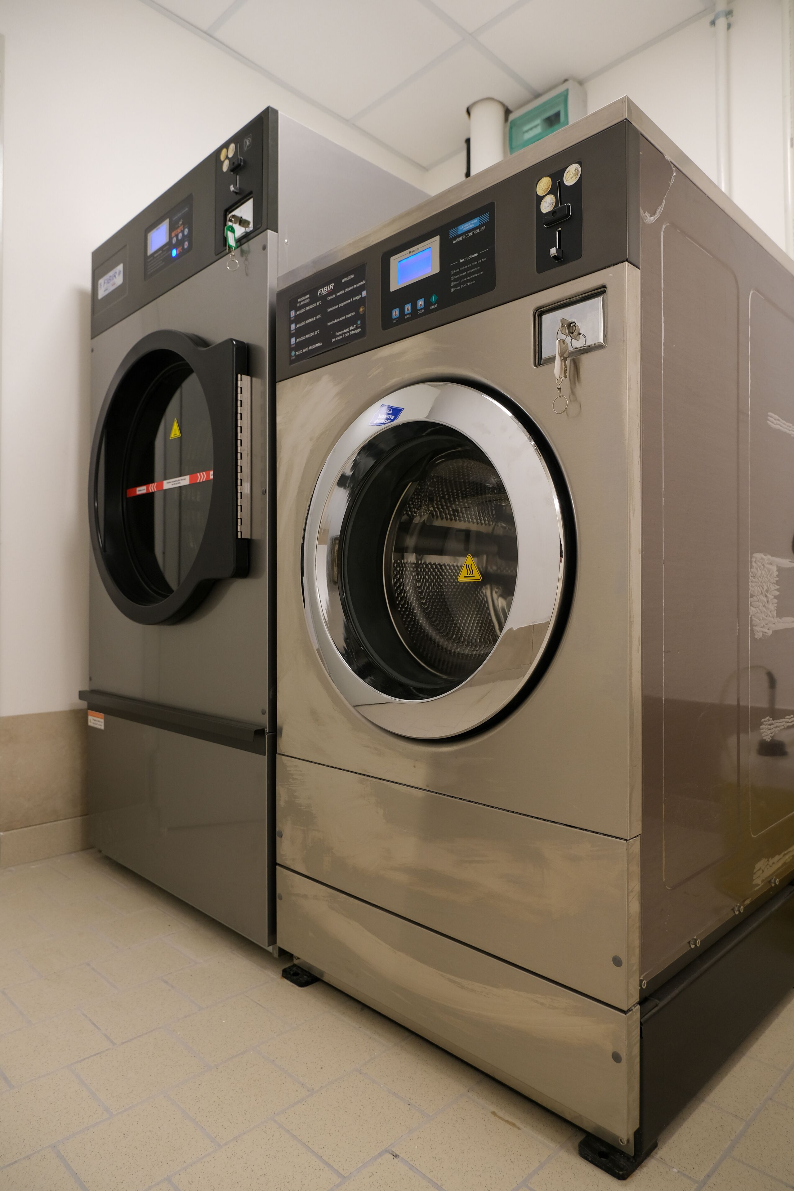 A large industrial-style washing machine with a digital display and control panel, placed in a clean, tiled room.