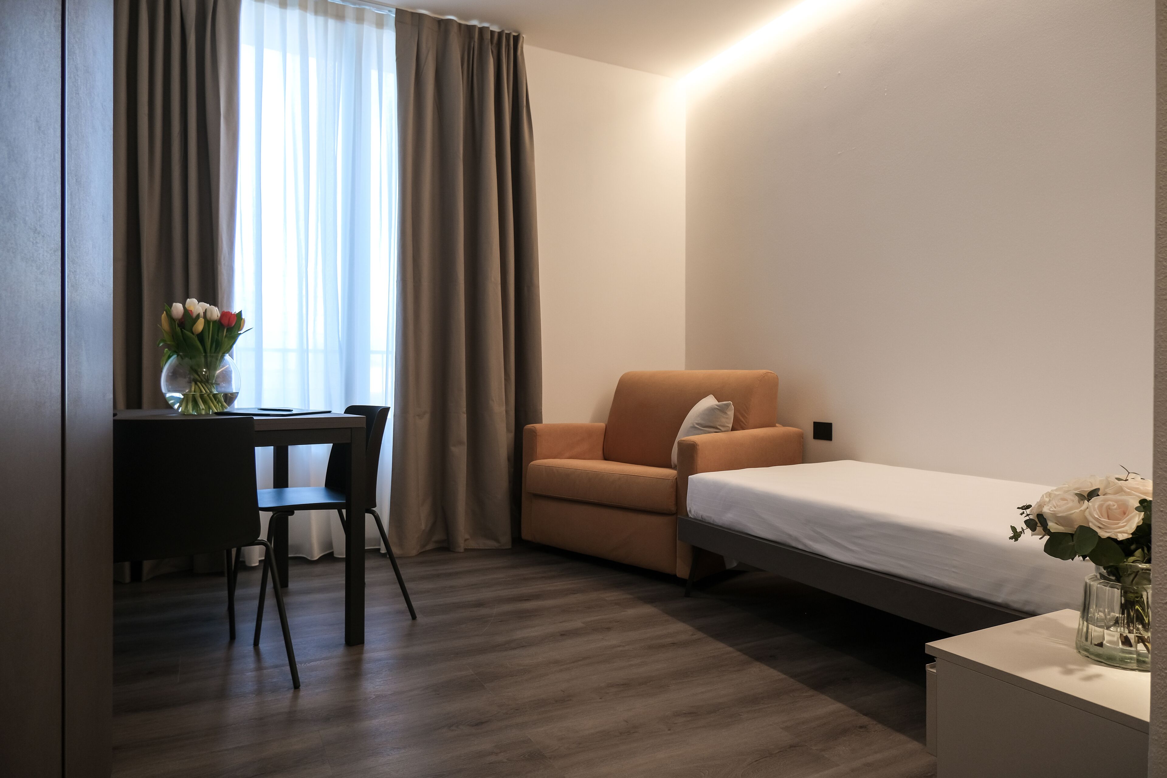 Ein Hotelzimmer mit Bett, Schreibtisch mit Stuhl, einer Couch und einem Fenster mit Vorhängen.