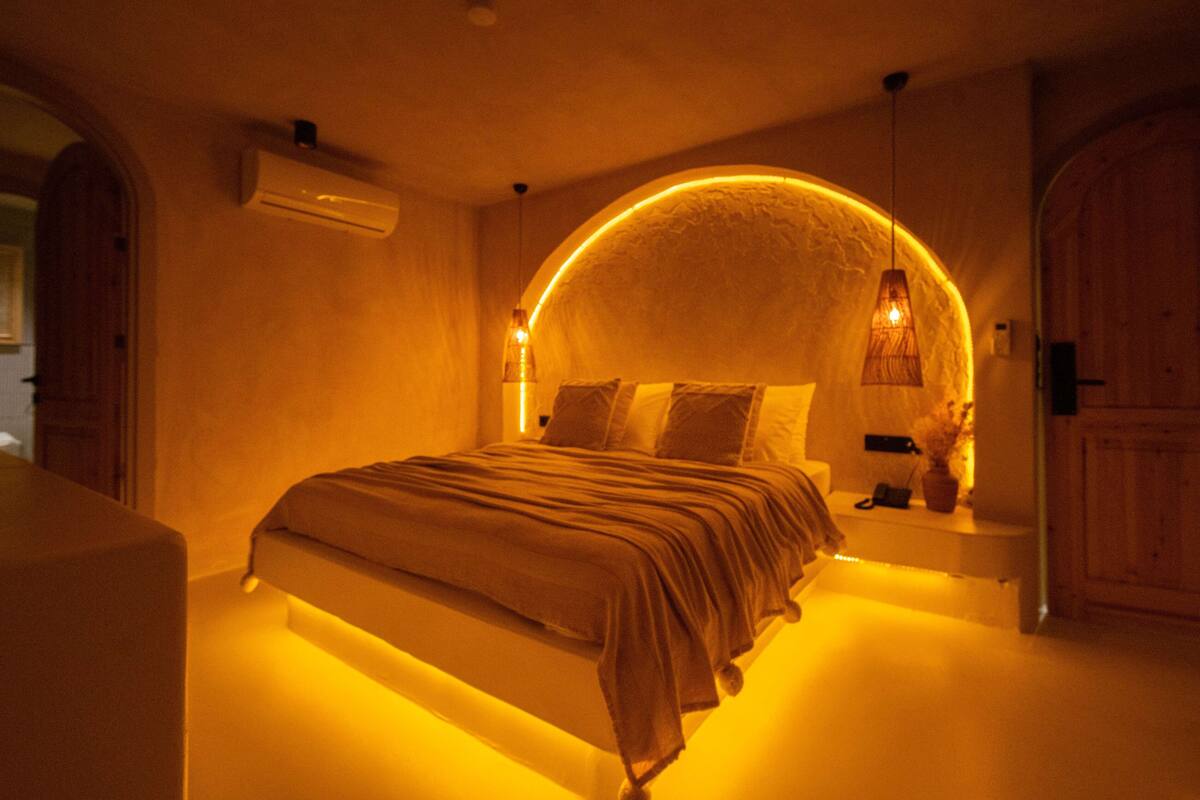 A bedroom with a curved ceiling, a bed with a headboard, and a bedside table with a lamp.