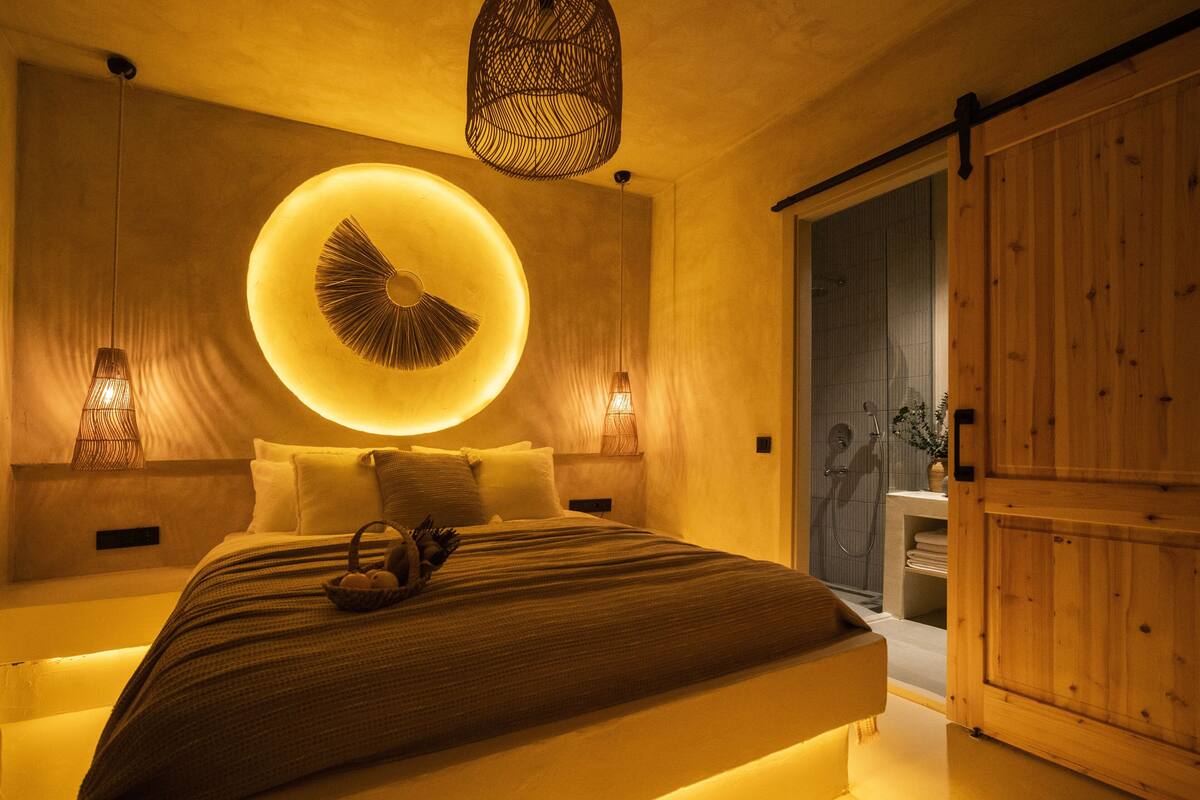 A modern bedroom with a large bed, a circular light fixture above the bed, and a wooden wardrobe.