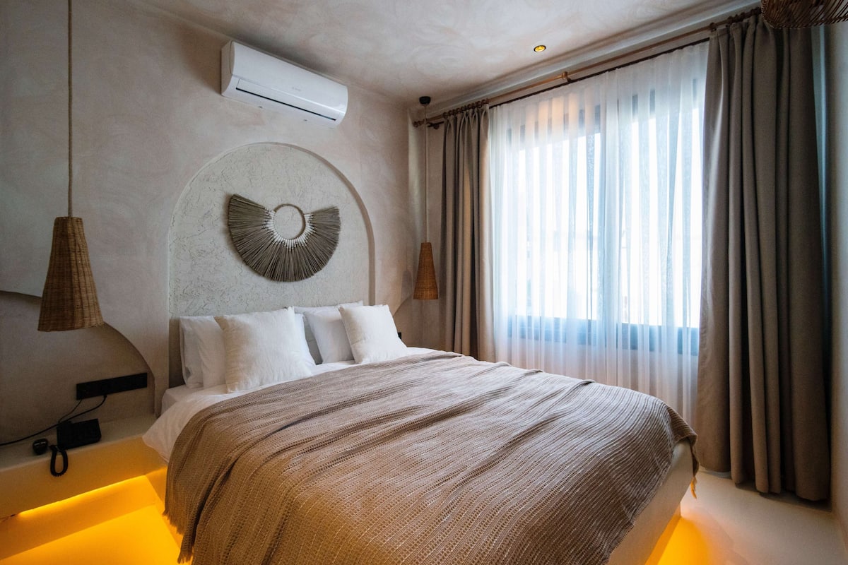 A modern hotel room with a large bed, a circular wall decoration, and a large window with curtains.