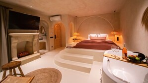 Un dormitorio con chimenea, una cama grande, una bañera y una bandeja con vasos y fruta.