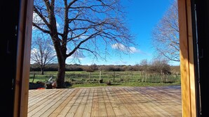 A wooden deck with a clear view of a rural landscape, including trees and a fence.