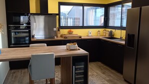 A modern kitchen with a wooden table, black cabinets, stainless steel appliances, and a window with a view of the outside.