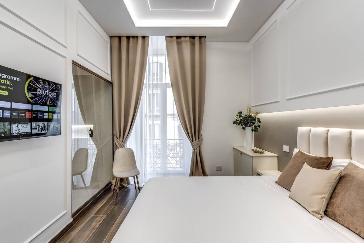 A modern hotel room with a large bed, a television mounted on the wall, a desk, and a chair.