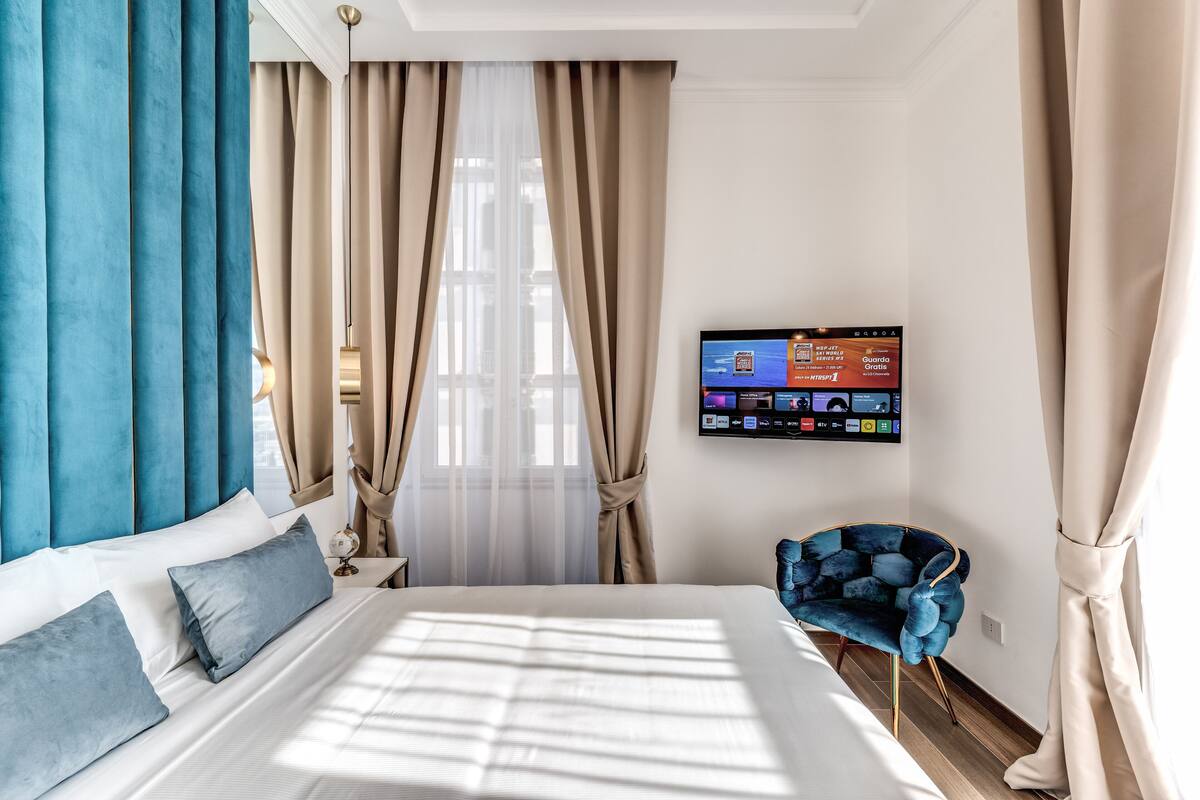 A hotel room with a large bed, a TV mounted on the wall, and a blue chair.