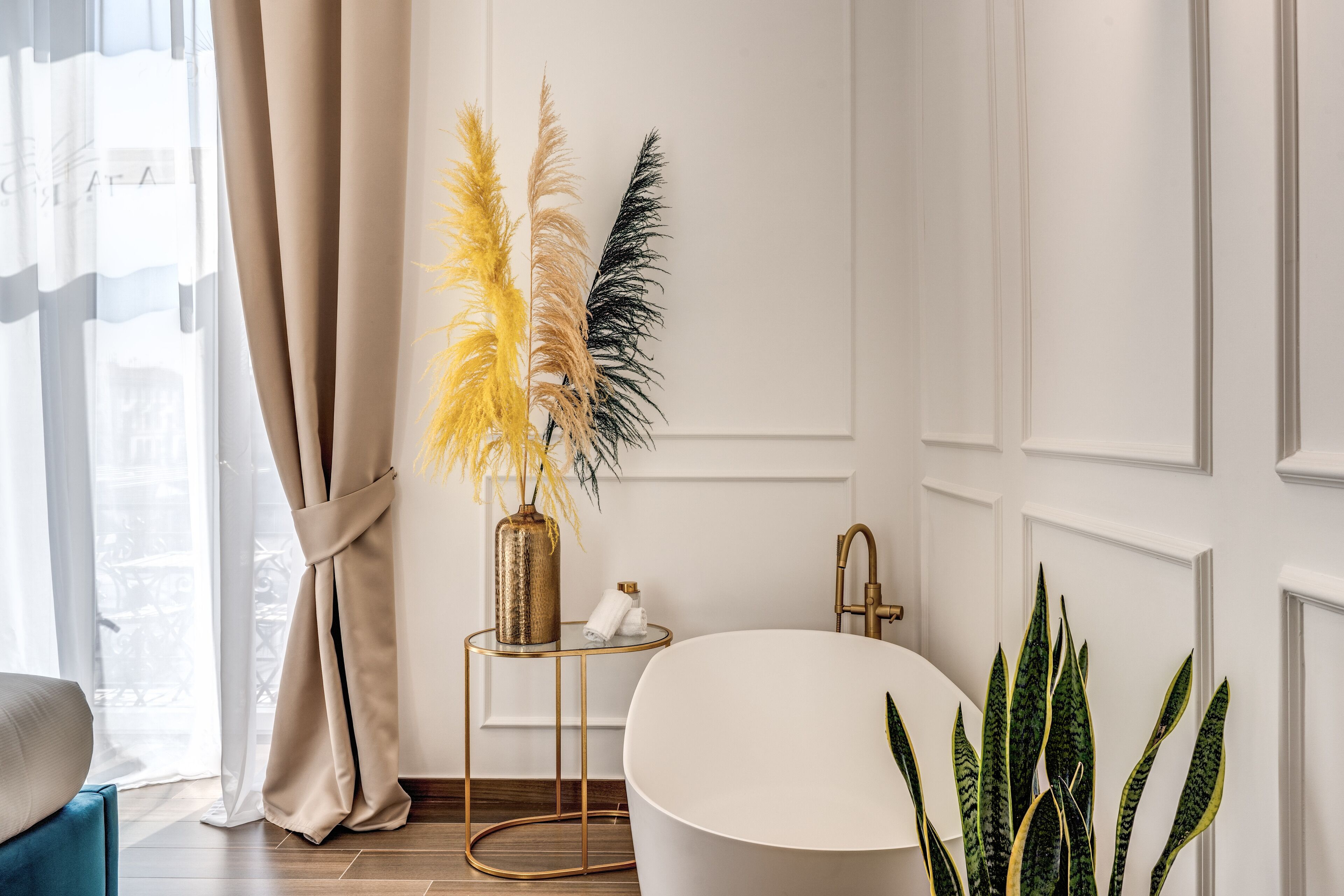 A modern bathroom with a white bathtub, a gold-framed vanity, and a potted plant.