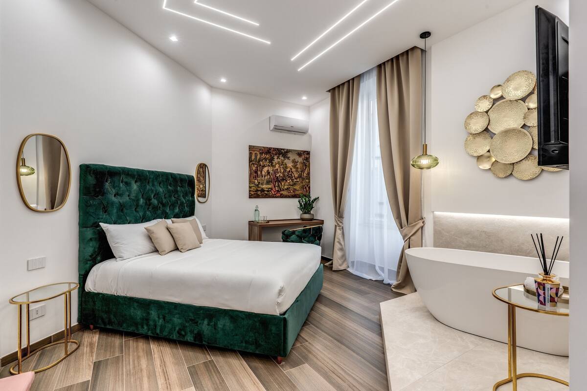A modern bedroom with a green upholstered bed, a white sofa, and a curved bathtub.