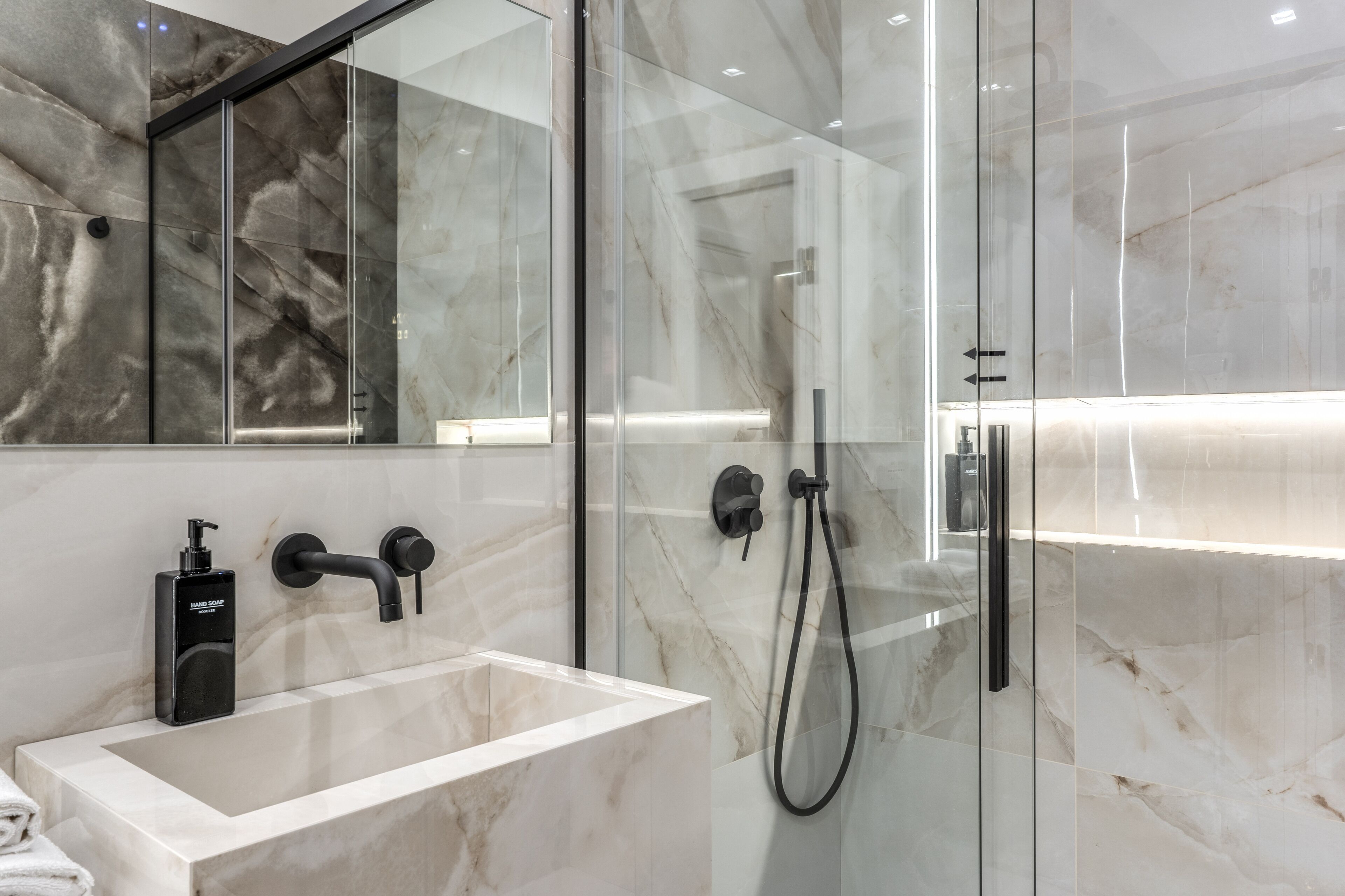 A modern bathroom with a glass-enclosed shower, a marble sink, and a handheld showerhead.